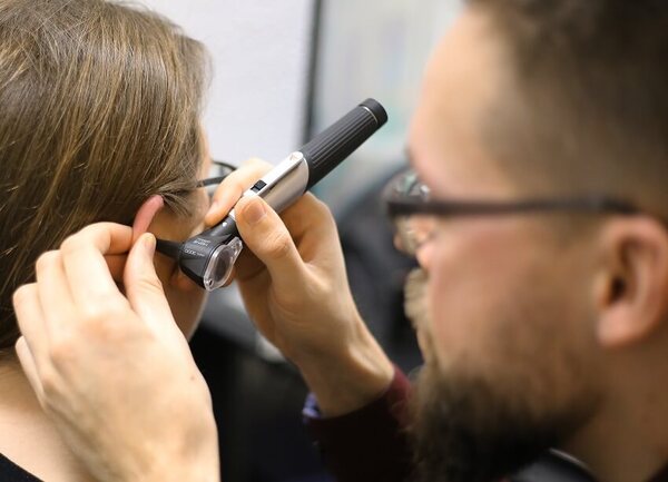 Ein HNO-Arzt untersucht mit einem Otoskop das Ohr einer Patientin in der Praxis.