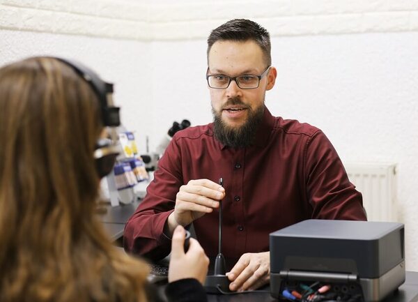 Hörtest beim Hörakustiker: Mann erklärt einer Frau die Bedienung eines Hörtestgeräts.