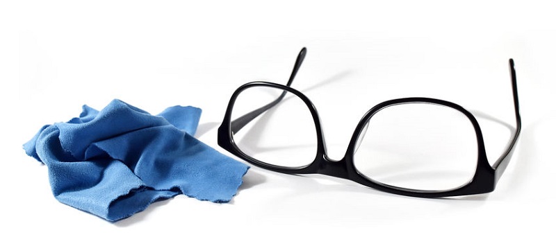 Schwarze Brille neben blauem Mikrofasertuch zur Brillenreinigung auf Weiß